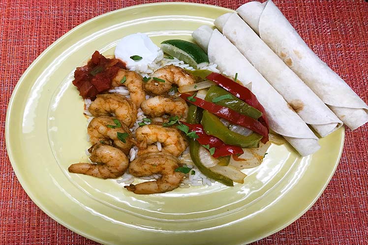 Gulf shrimp fajitas with peppers and onions beside soft flour tortillas.