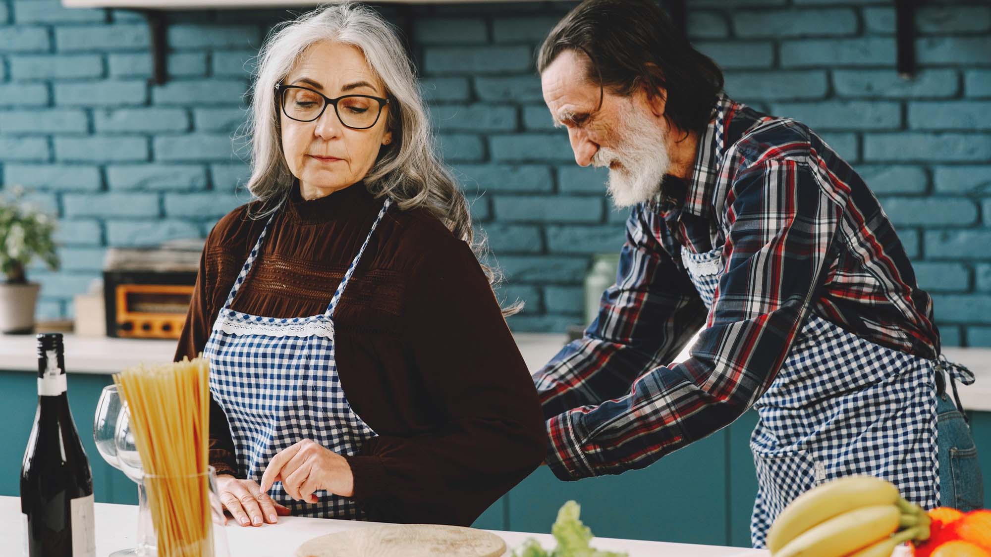 senior-couple-putting-on-aprons-in-kitchen-for-cooking-safely
